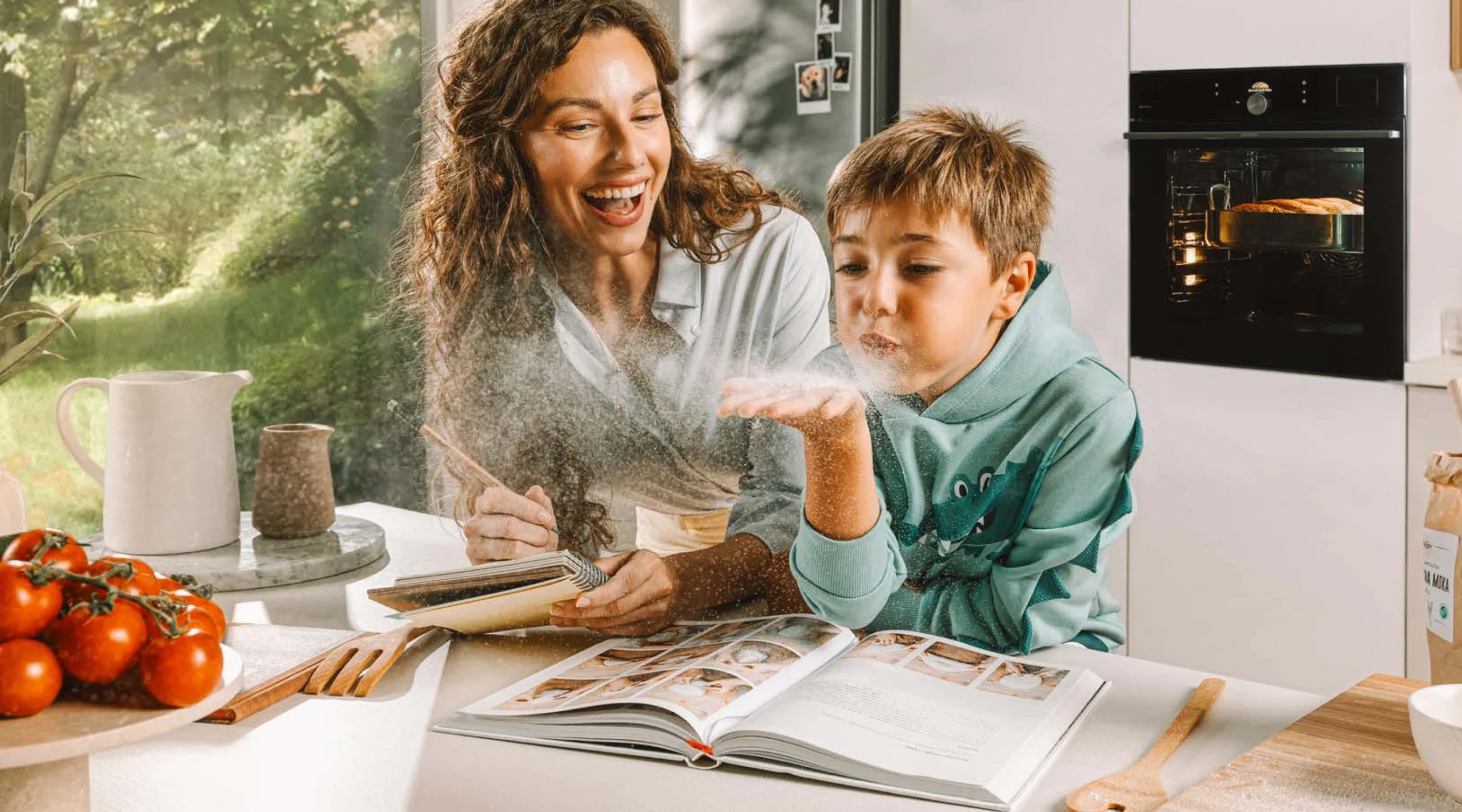 Mãe e filho brincando com farinha sobre um livro de receitas na cozinha